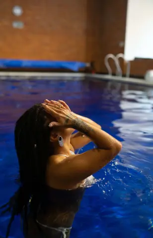 Woman with long braids in a dark swimsuit relaxing in a blue swimming pool on a sunny day.