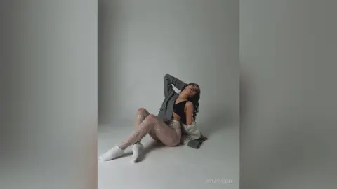 Fashionable woman in a black crop top and patterned leggings sitting in a minimalist studio setting.