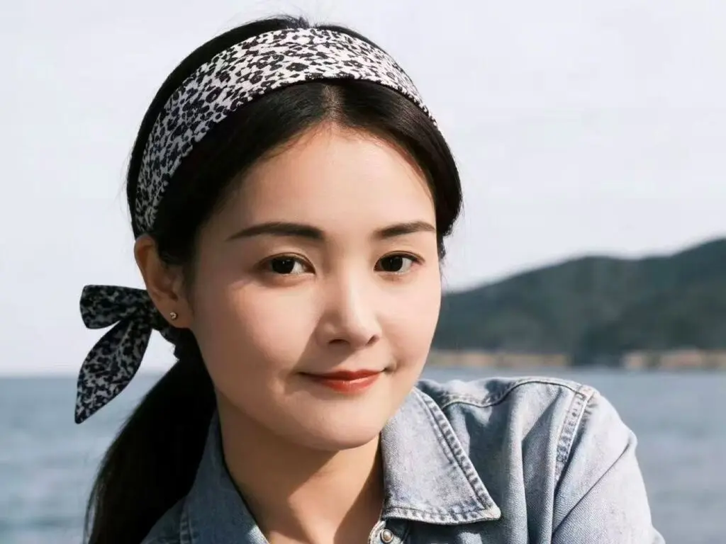 Smiling young woman in a denim shirt and patterned headband relaxing by the ocean on a sunny day.