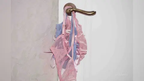Pink lace lingerie hanging on a brass door handle against a neutral textured wall.