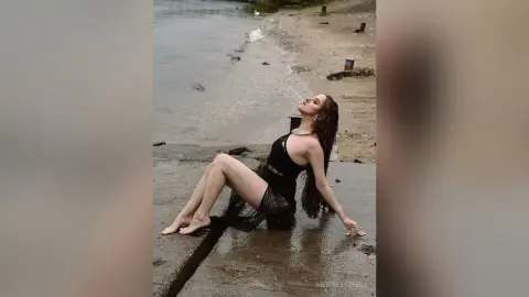 Elegant woman in a black lace dress sitting on a wet pier by the ocean under a moody sky.