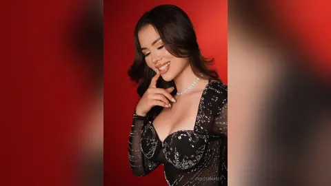 Smiling woman in a glamorous black sequin dress posing against a vibrant red background.