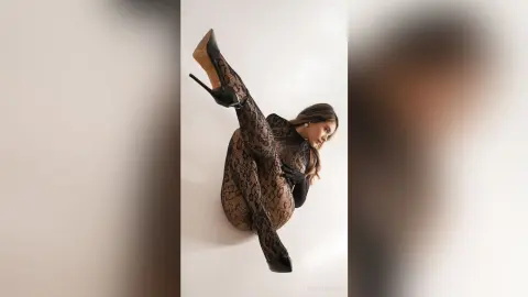 RosieThomas — RosieThomas poses in a black snakeskin print bodysuit and high heels, showing off her long hair and legs against a plain white background.