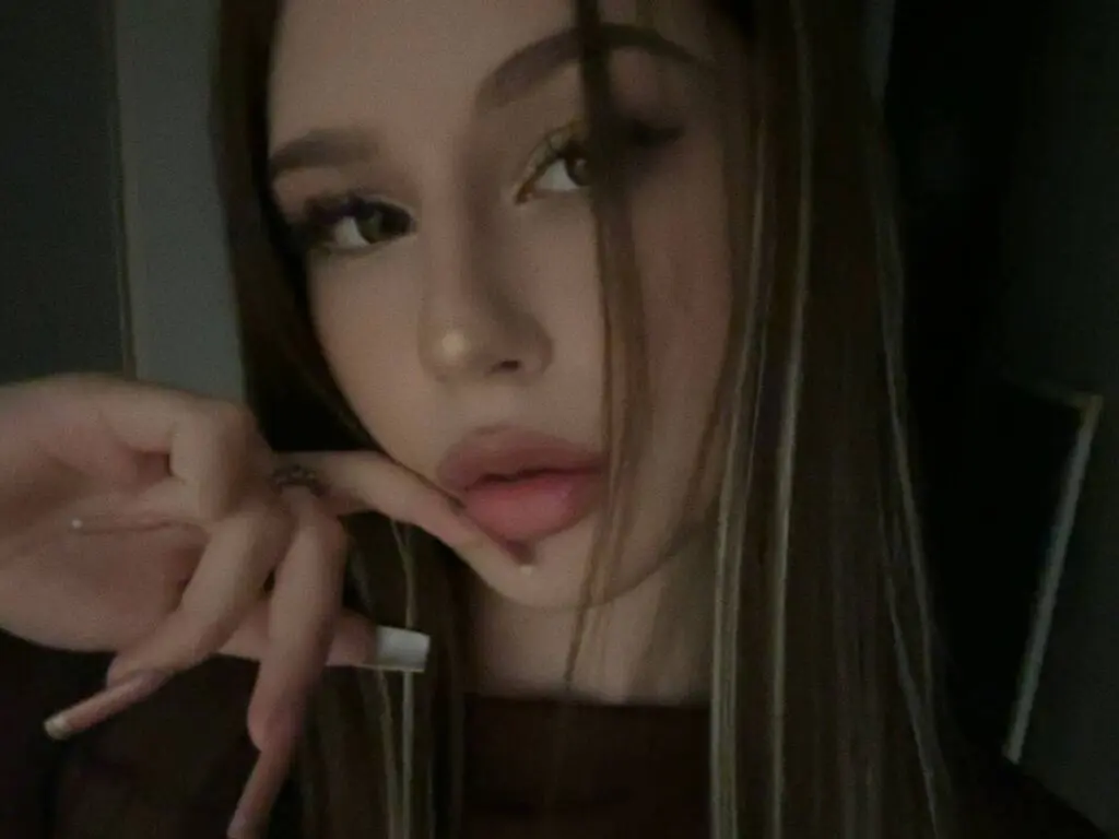 KathlineVelzy poses close-up, resting her hand under her chin and looking at the camera with long hair and heavy eye makeup.