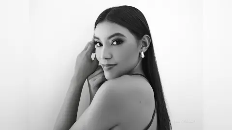Elegant woman with long dark hair and hoop earrings posing in a minimalist black and white portrait.