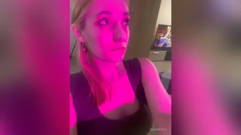 Young woman in a black tank top posing under moody pink neon lighting in a dimly lit room.