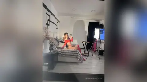 Young woman in a red outfit taking a mirror selfie in a modern, minimalist bedroom setting.