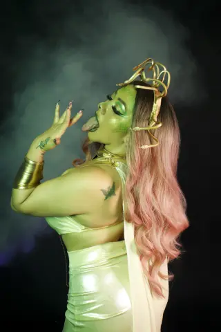 Woman in shimmering white gown and gold crown posing with mystical green lighting and smoky background.