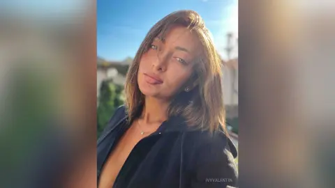Young woman in a black top posing outdoors under bright sunlight with a serene expression.