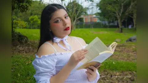 Young woman in a white off-the-shoulder top reading a book in a peaceful green park setting.