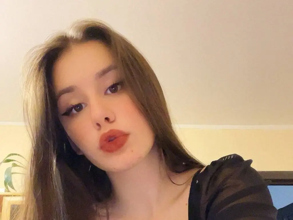 Young woman with long brown hair wearing a black top in a warm, indoor setting.