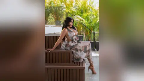 DayanaHille sits on brown wooden steps wearing a patterned sleeveless dress and tan high heels.