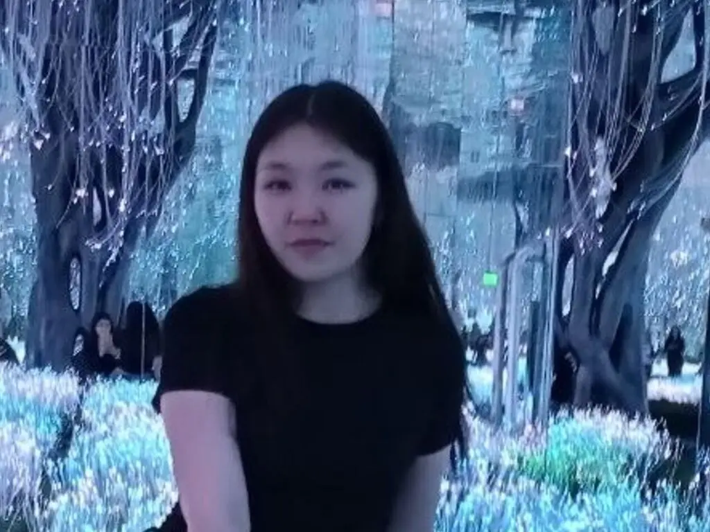 Young woman in a black t-shirt sitting in a dreamy, ethereal blue forest setting with magical lighting.