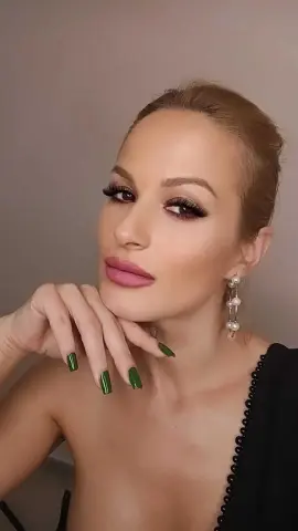 Elegant woman with glamorous makeup and pearl earrings wearing a black beaded dress in a soft studio setting.