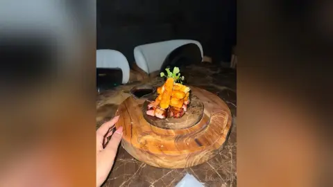 Gourmet appetizer platter with crispy fried toppings and dipping sauce served on a rustic wooden board in a dim restaurant.