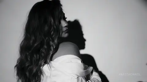 Moody black and white portrait of a woman with long wavy hair wearing an off-the-shoulder white blouse.