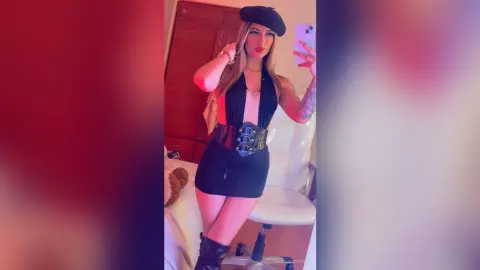 Stylish woman in a black halter dress and beret taking a selfie in a warm, moody indoor setting.