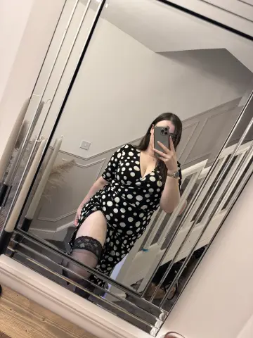 Woman in a black and white polka dot midi dress posing in a mirror for a stylish indoor selfie.