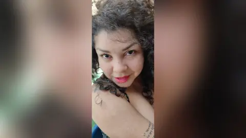 Smiling woman with curly hair wearing a black top in a bright, natural outdoor setting.