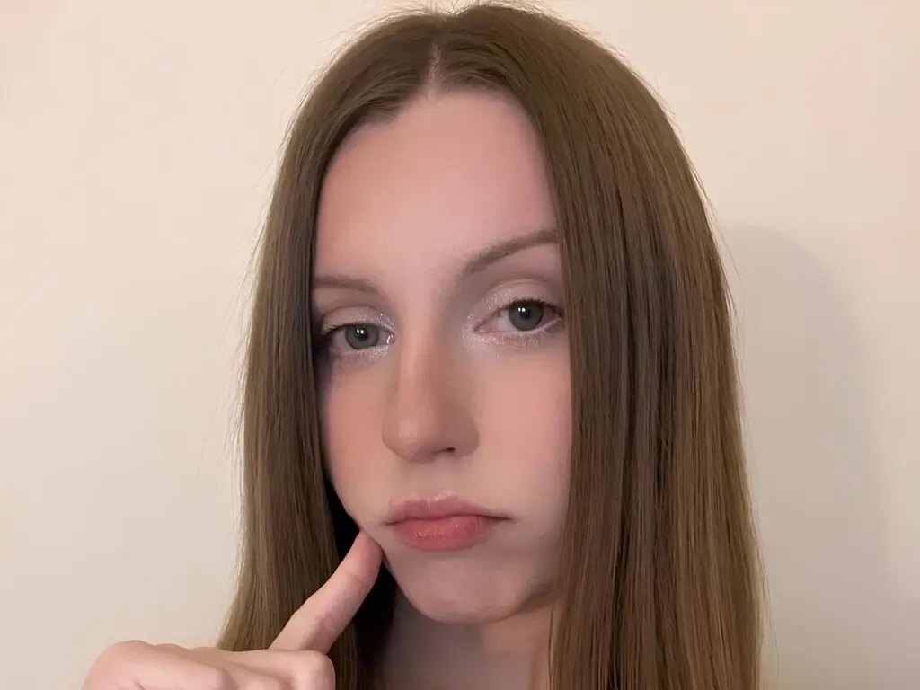 Young woman with long straight brown hair and natural makeup posing against a plain white wall.