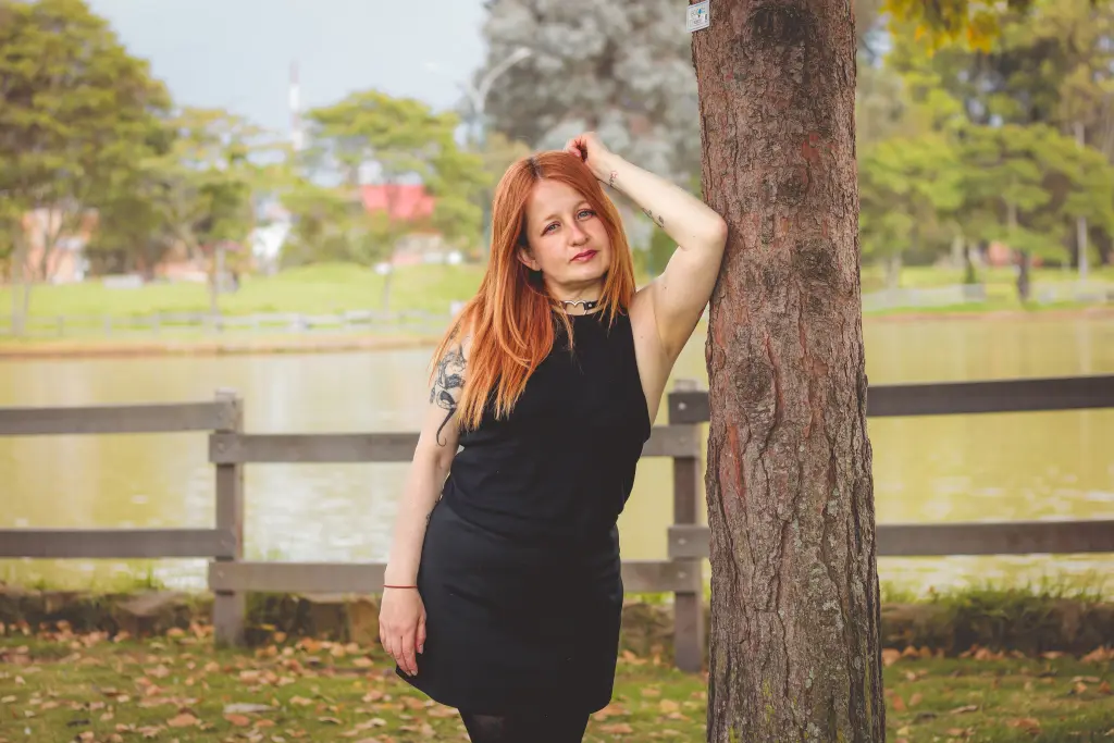 ViiolettaMora poses with long red hair, wearing a black lace top and a black choker against a soft-focus background.