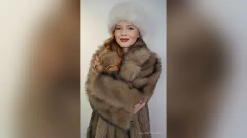 Elegant woman in a luxurious brown faux fur coat and white fluffy hat posing against a white background.