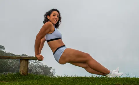Fit woman in light blue sports bra and briefs leaning on a wooden bench in a misty, foggy outdoor landscape.