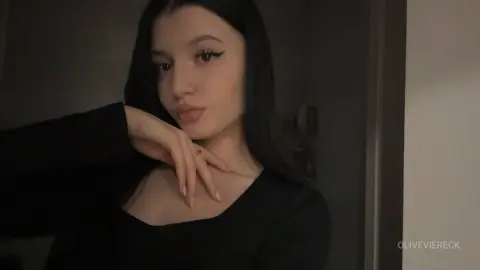 Young woman with dark hair and winged eyeliner wearing a black top in a moody indoor setting.
