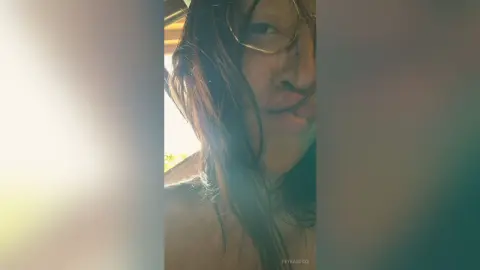 Close-up portrait of a woman with long hair wearing glasses in soft, warm natural lighting.