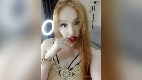 Blonde woman in a lace beige camisole posing with red lipstick in a bright indoor setting.