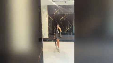 Stylish woman in a grey blazer and mini skirt posing in a modern black marble lobby.