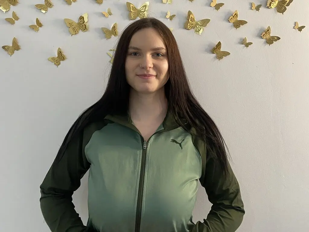 Young woman in a green Puma zip-up jacket standing against a white wall decorated with gold butterfly decals.