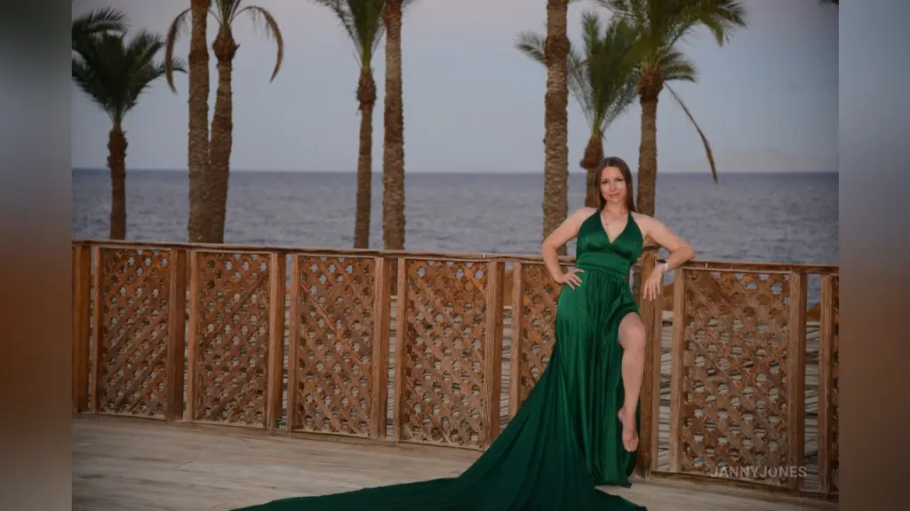Elegant woman in a flowing emerald green evening gown posing on stone stairs at a luxury villa during sunset.