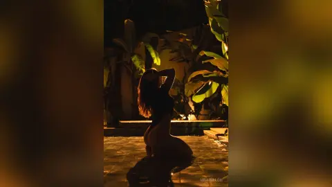 MilaWillow poses naked in a dark outdoor pool surrounded by tropical plants at night.