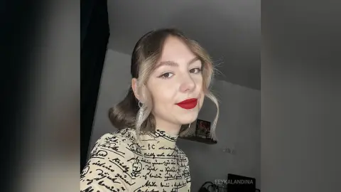 Young woman with blonde wavy hair and red lipstick wearing a black and white script print turtleneck top.