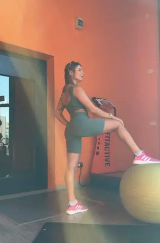 Fit woman in olive green gym wear stretching her leg on a yoga ball in a bright fitness studio.