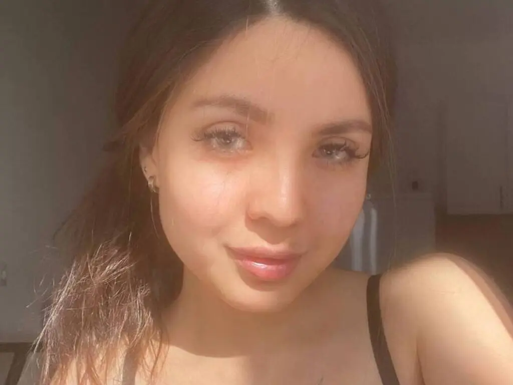 Close-up portrait of a smiling young woman with long brown hair in soft natural sunlight.