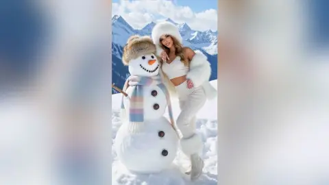 Smiling woman in white winter outfit posing with a snowman in a snowy mountain landscape.