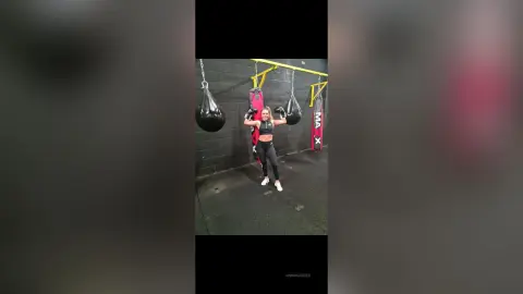 Athletic woman in black gym wear training with heavy punching bags in a moody boxing gym.
