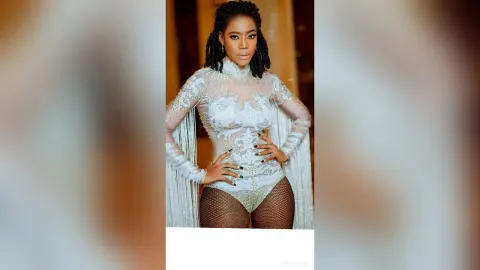 Elegant Black woman in a glamorous white sequined bodysuit with fringe detailing posing in a luxury setting.