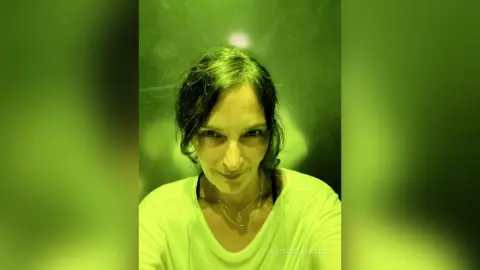 MichaelaBelle smiles at the camera wearing a white t-shirt with her dark hair pulled back.