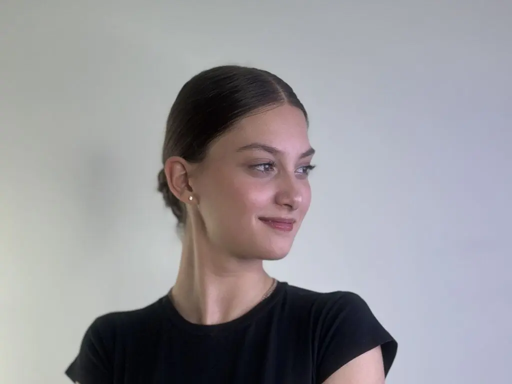 Smiling young woman in a black t-shirt posing against a minimalist white background.