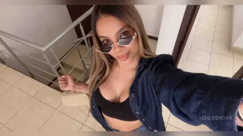 Young woman in a black crop top and denim jacket holding a small beige purse on a tiled staircase.