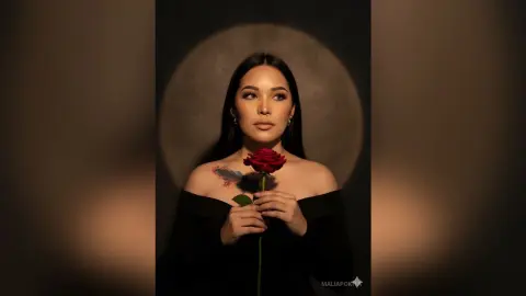 Elegant woman in a black off-the-shoulder dress holding a red rose against a moody, circular backlit background.