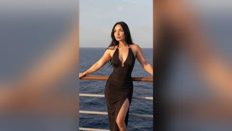 Elegant woman in a black evening gown posing on a ship deck against a serene ocean sunset backdrop.