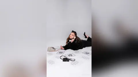 Fashionable woman in a black outfit lying on a white floor with vintage telephones and text cards.