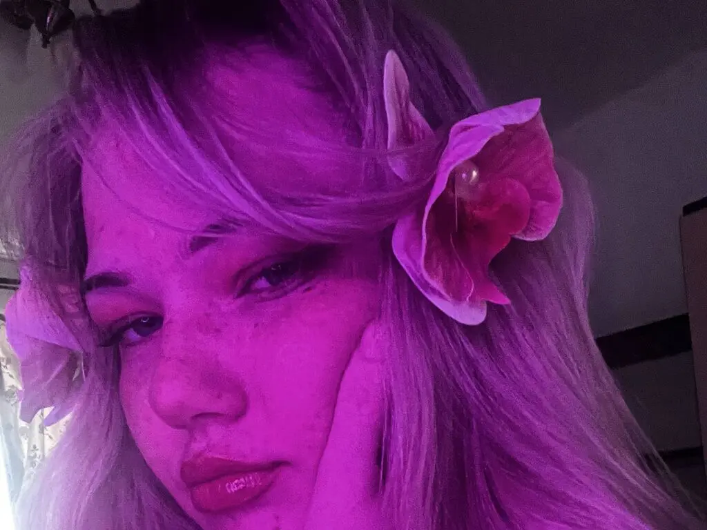 Close-up portrait of a girl with pink hair and a flower accessory in dreamy purple lighting.
