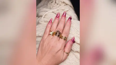 Close-up of a hand with pink ombre floral nail art wearing vintage gold rings against a cozy white sweater.
