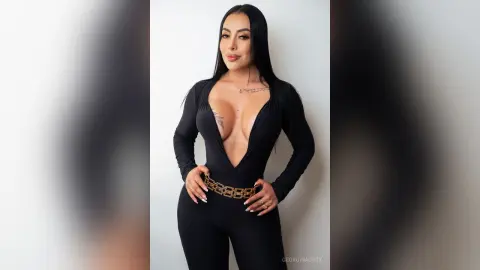 Confident woman in a sleek black long-sleeve bodysuit with a gold chain belt posing against a white background.