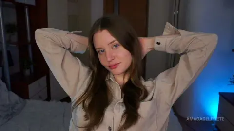 Young woman in a beige linen shirt relaxing in a cozy, dimly lit bedroom setting.